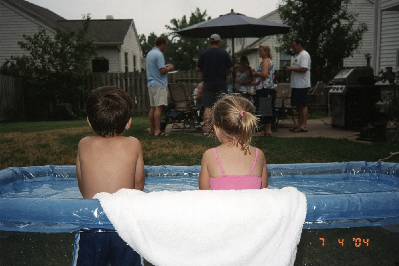 Flash snapshot of two children at a backyard pool in 2004, shot from behind with a date stamp